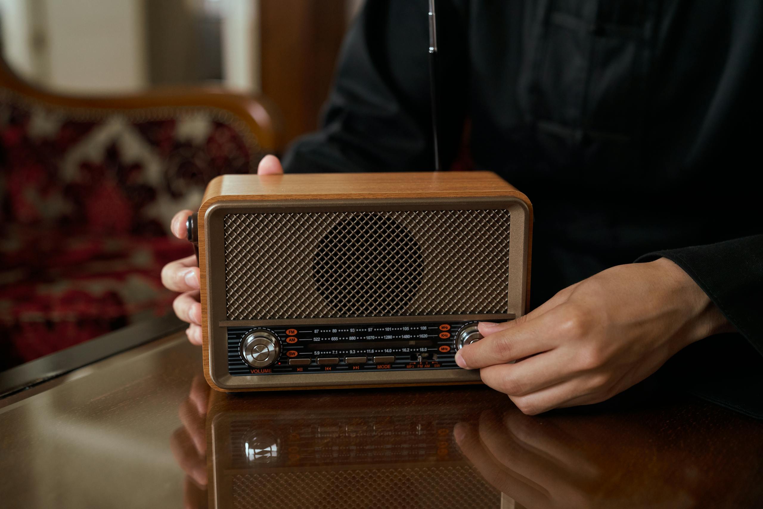 Person adjusting vintage wooden radio knob, close-up indoor shot.
