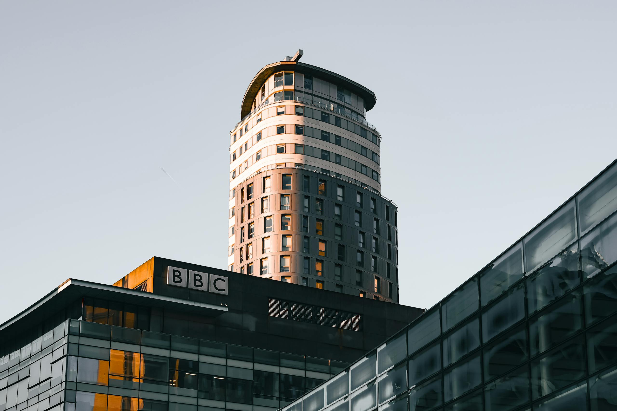 Modern architecture of the BBC building at Salford Quays, highlighted by warm sunlight during the golden hour.