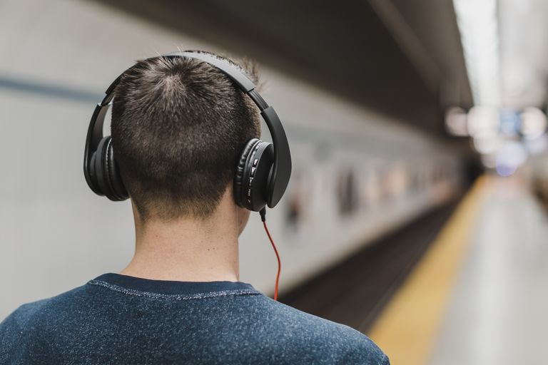 Back view of a young man with headphones listening to music in a subway station.