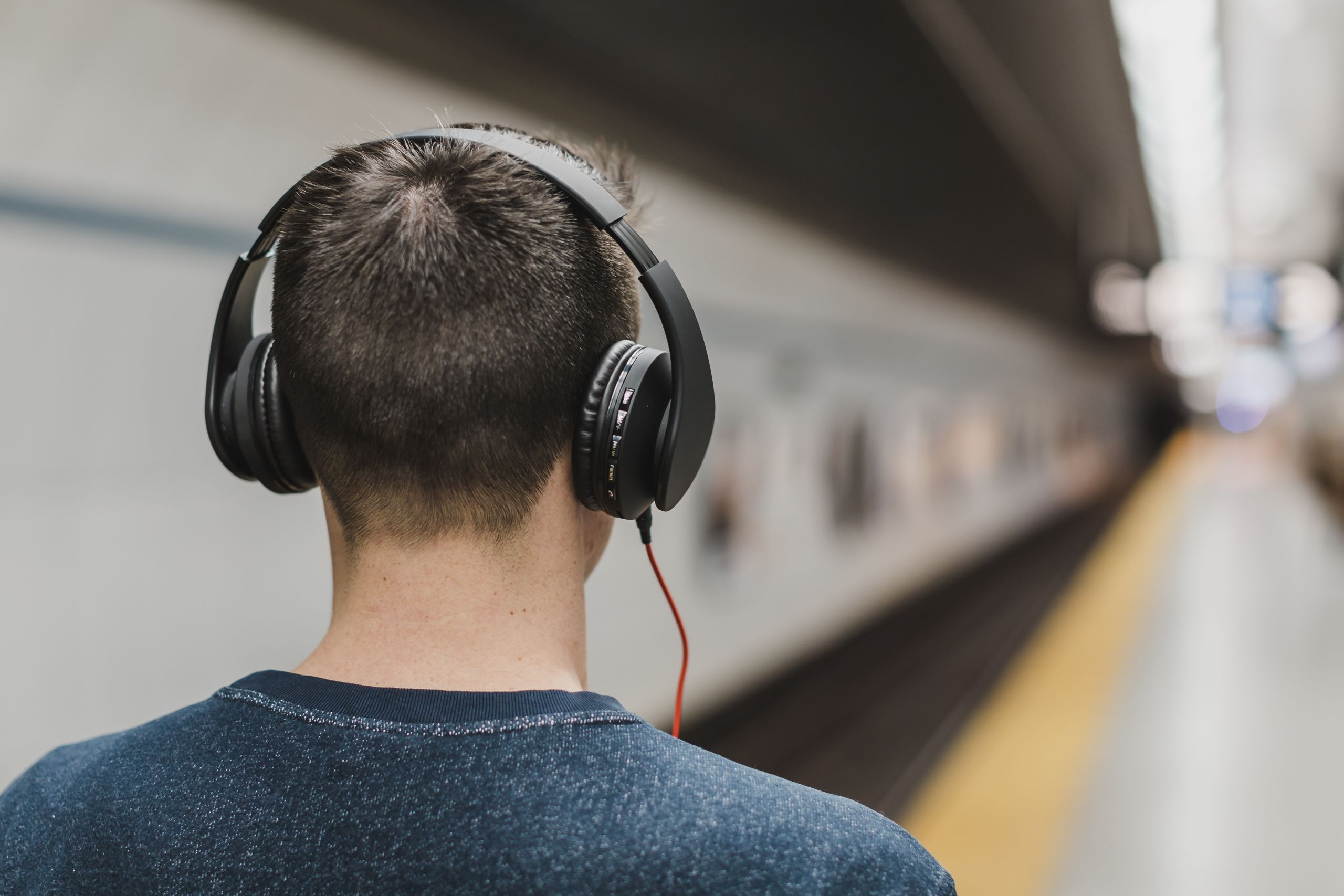 Back view of a young man with headphones listening to music in a subway station.